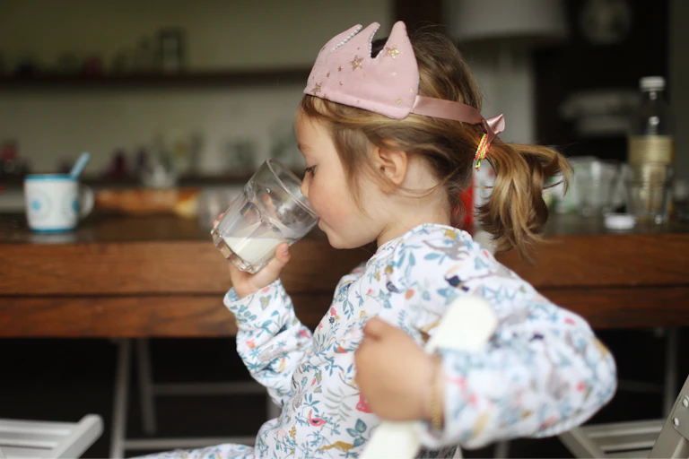 Child wearing a toy crown drinks milk at her kitchen table
