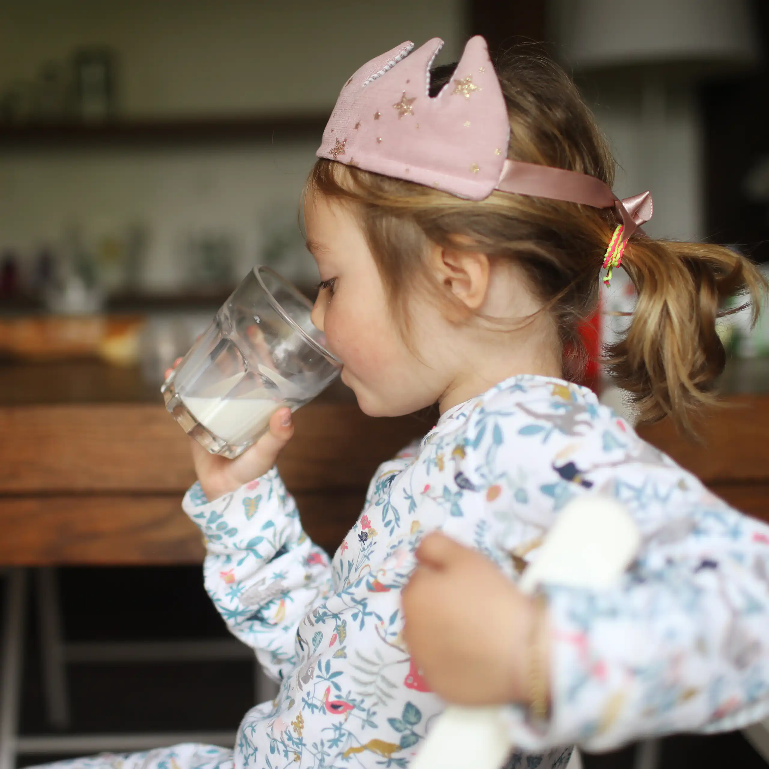 Child wearing a toy crown drinks milk at her kitchen table