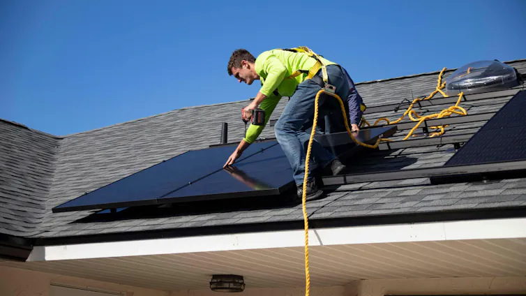 A man installing solar panels on a house roof
