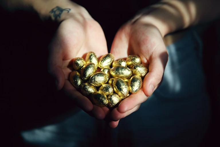 Person holding gold-foil covered, small Easter eggs in palms stretched out
