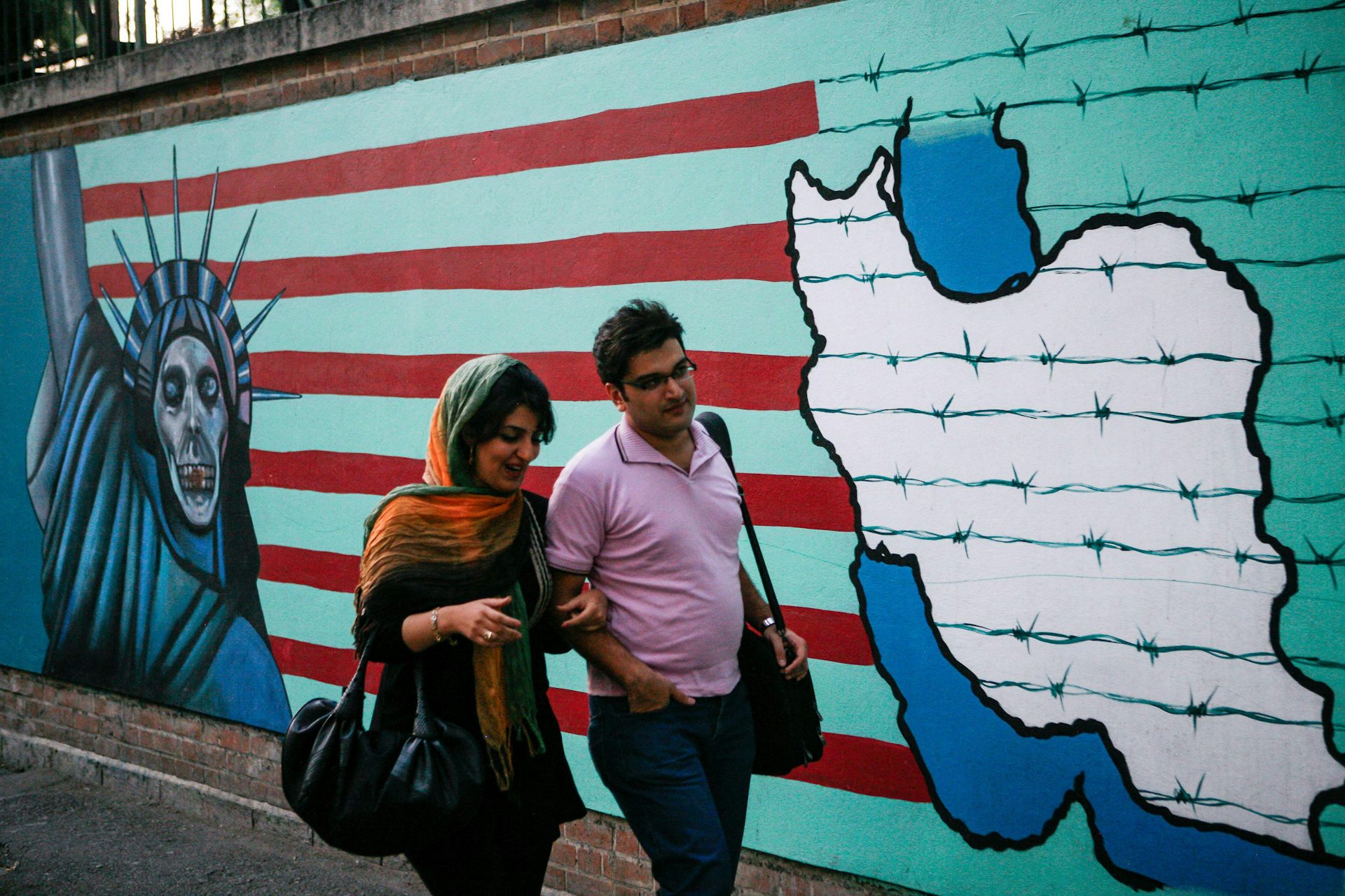 A man and woman walk past an anti-US mural on the walls of the former US embassy in Tehran.