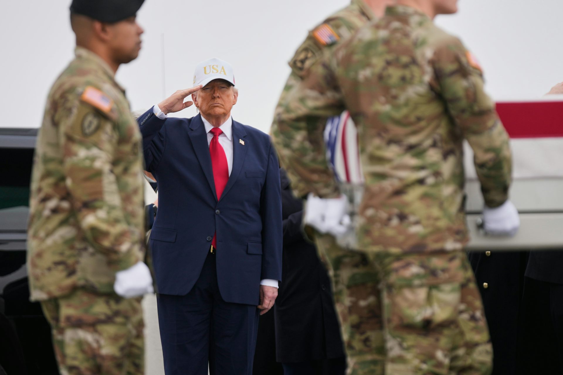 Un hombre corpulento con traje azul, corbata roja y gorra blanca saluda.