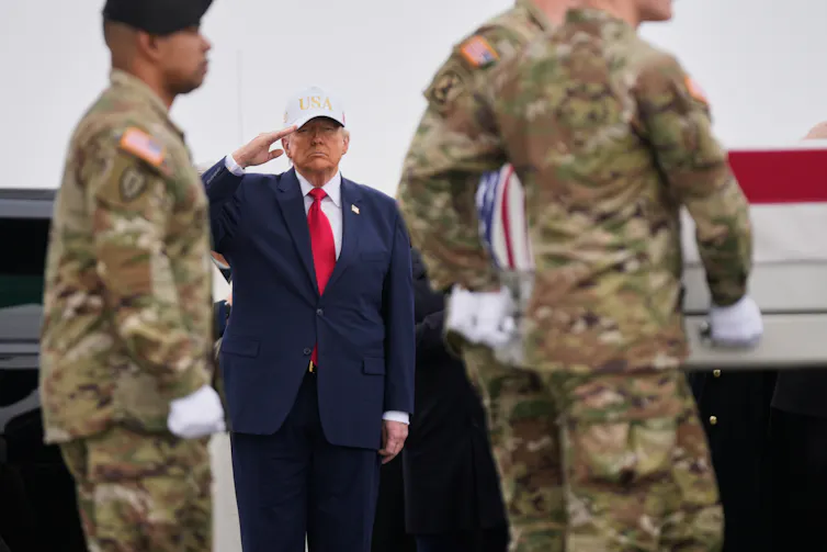 Un hombre corpulento con traje azul, corbata roja y gorra blanca saluda.