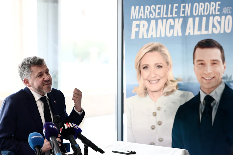 image d'un homme devant une affiche du Rassemblement National