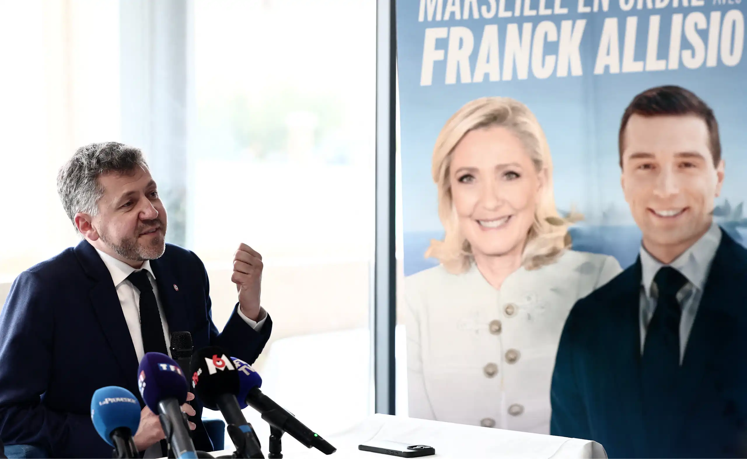 image d'un homme devant une affiche du Rassemblement National