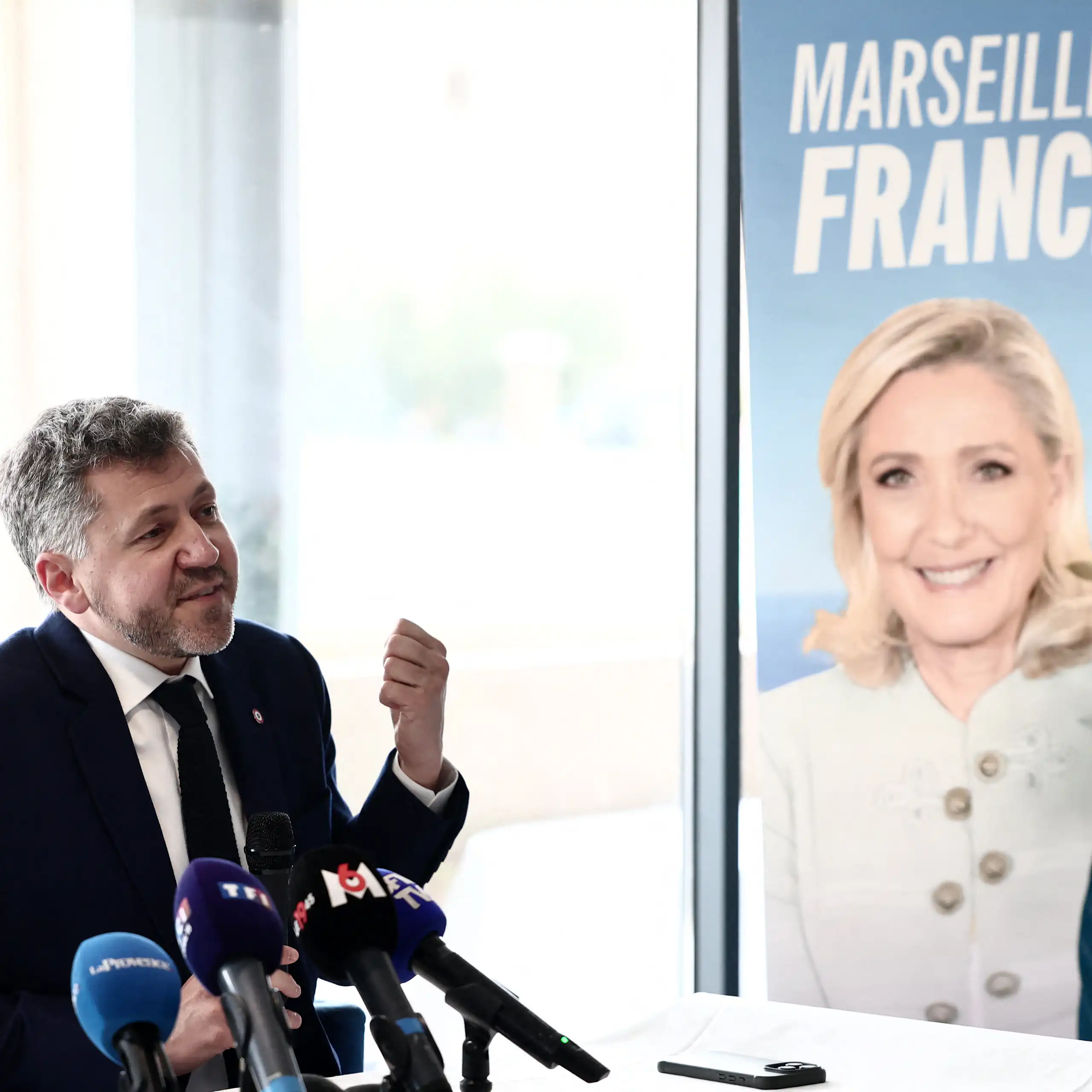 image d'un homme devant une affiche du Rassemblement National