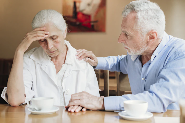 A man with gray hair comforting a woman with gray hair who is resting her forehead on her hand