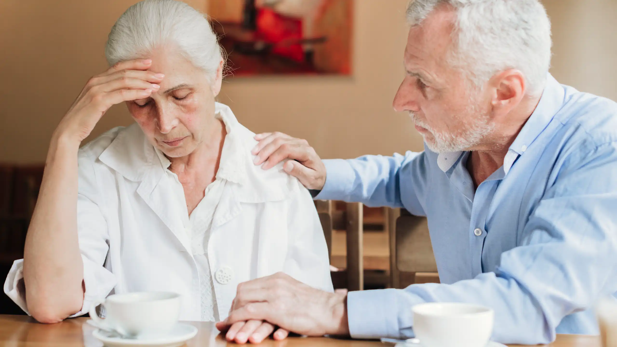 A man with gray hair comforting a woman with gray hair who is resting her forehead on her hand