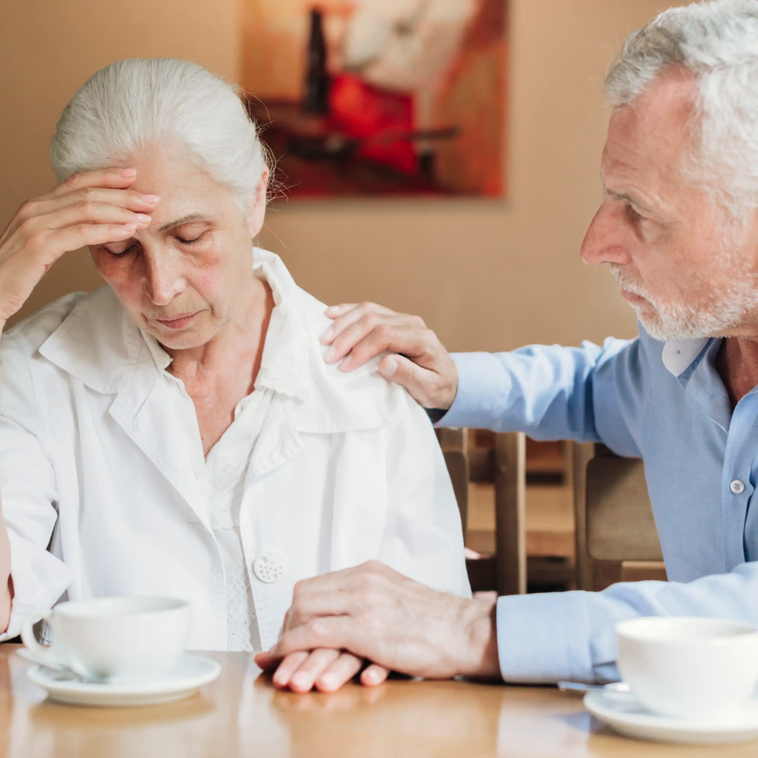 A man with gray hair comforting a woman with gray hair who is resting her forehead on her hand