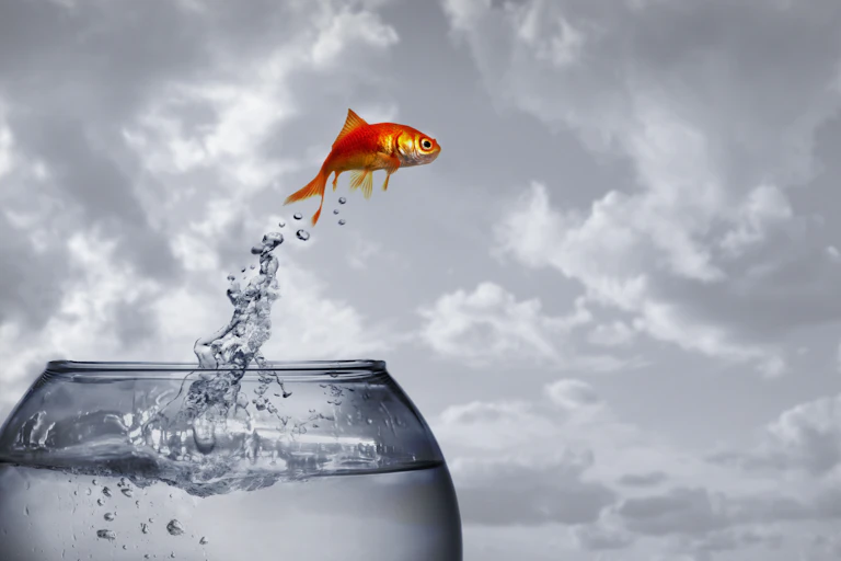 Goldfish leaping out of bowl against cloudy landscape.