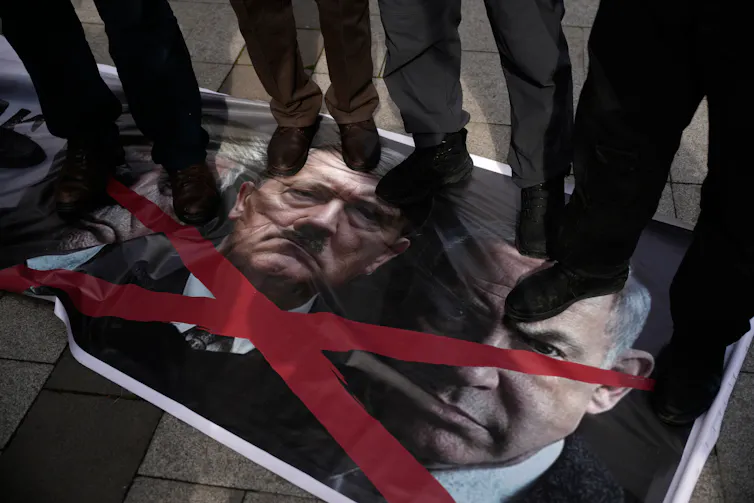 Personas arrodilladas se paran sobre fotografías de cabezas de dos hombres/