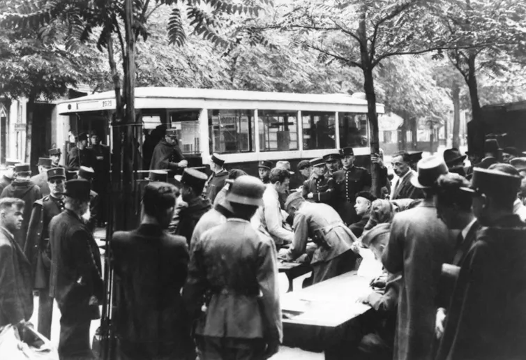 A black-and-white photo of a crowd, including many uniformed officers, standing outside by a trolley.