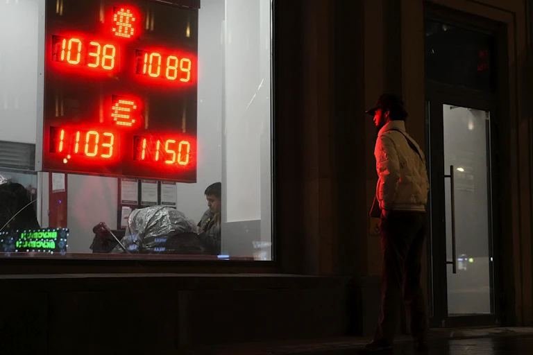 A man looks at an exchange office sign showing the currency exchange rates of the Russian ruble, U.S. dollar, and euro