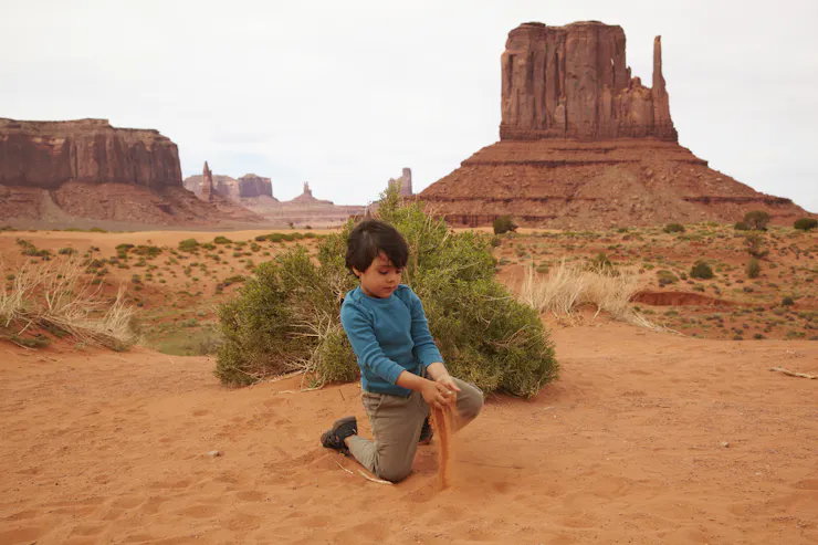 A child plays with sand in in front of a rock formation in Monument Valley