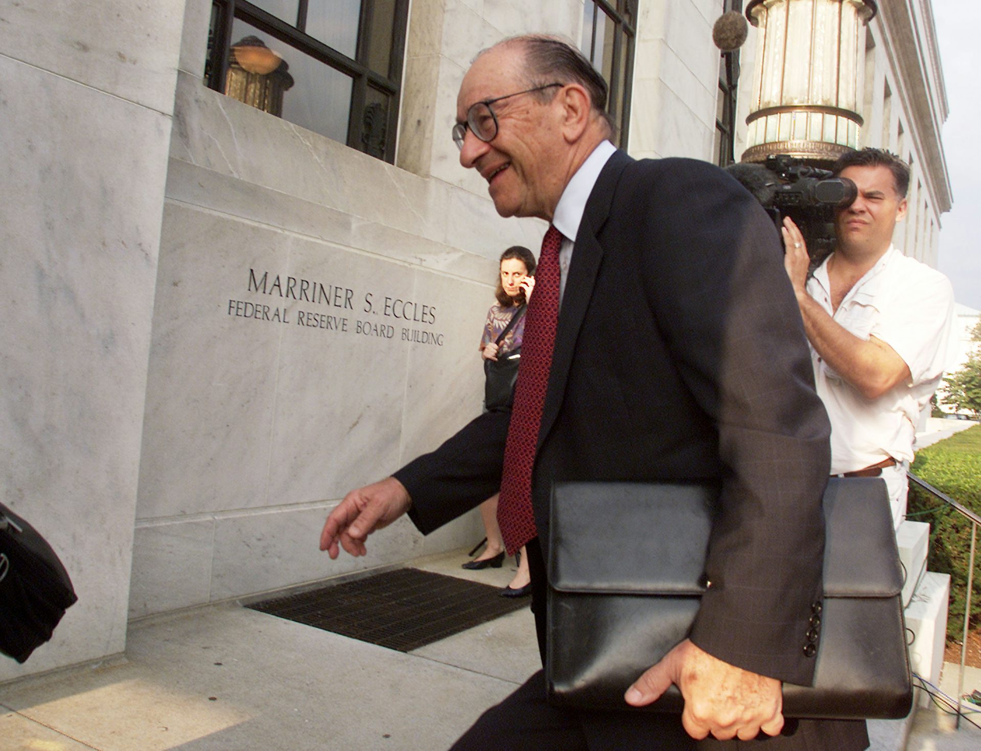 white man in a suit and carrying a black briefcase walks up the steps of a stone building
