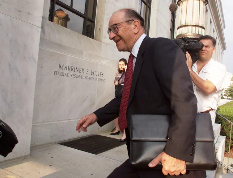 white man in a suit and carrying a black briefcase walks up the steps of a stone building