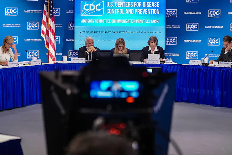 A panel of adults sit around a long table drenched in a blue tablecloth.