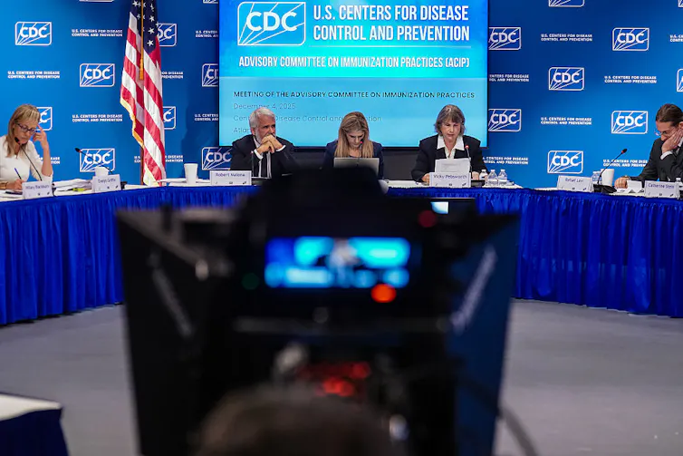 A panel of adults sit around a long table drenched in a blue tablecloth.