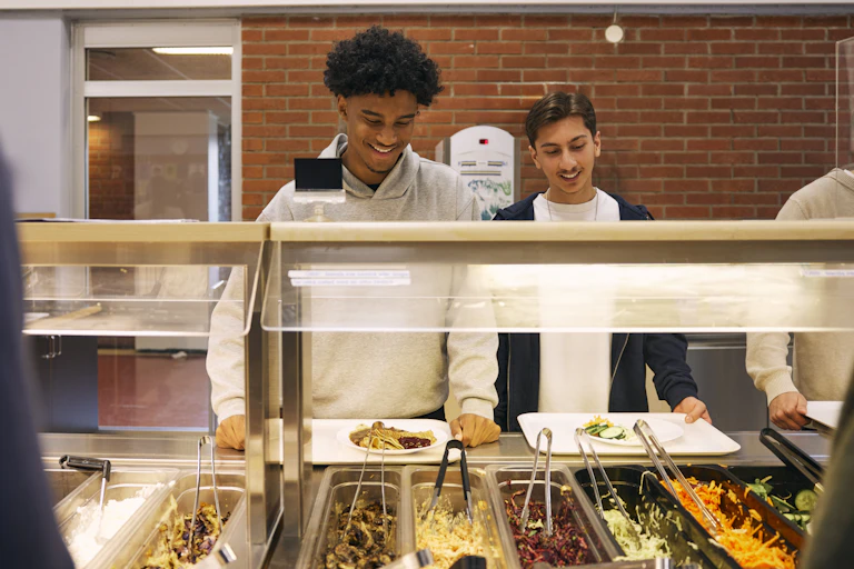 two teenagers with trays of food at a self-serve cafeteria display