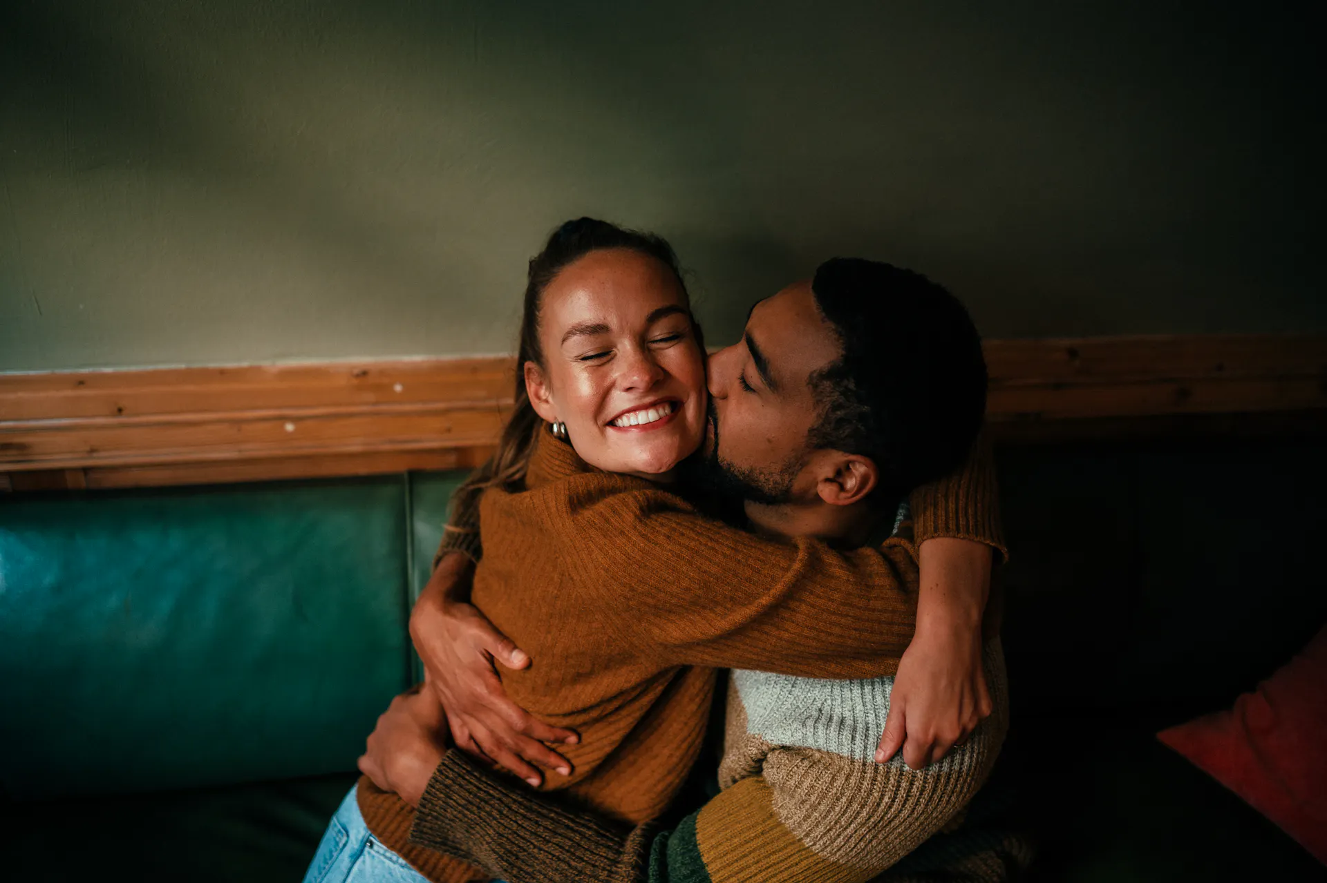 young couple embrace while man kisses smiling woman's cheek