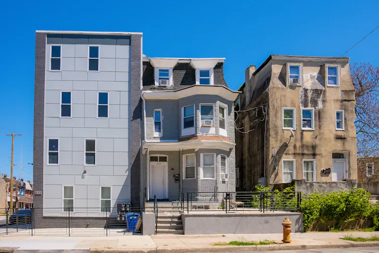 View of grey, boxy new construction building next to two older, more traditional houses