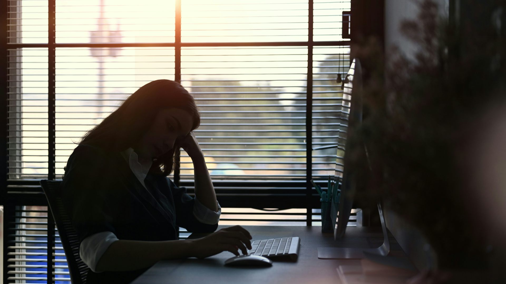 A woman sitting at a desk in an office with her head resting against her hand