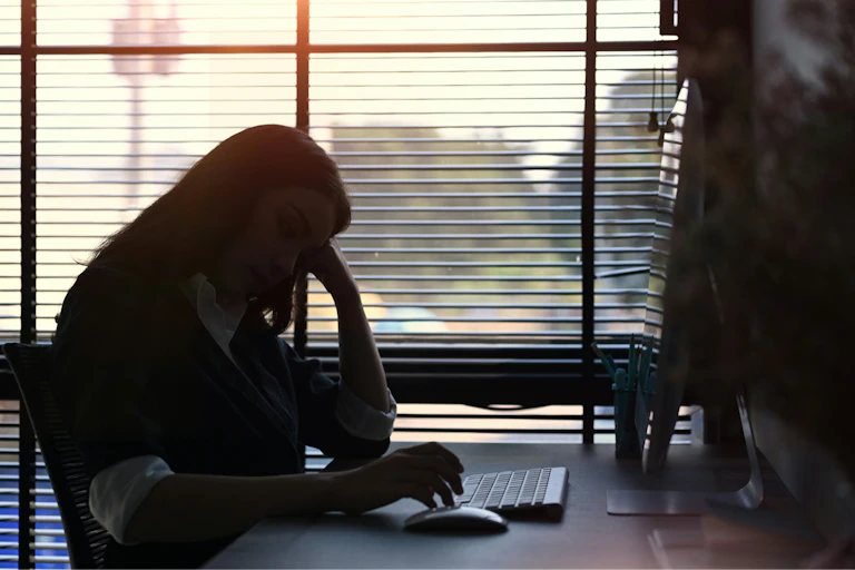 A woman sitting at a desk in an office with her head resting against her hand
