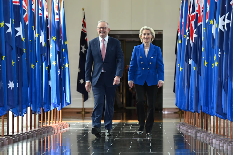 Anthony Albanese and Ursula von der Leyen walk through a hall between rows of flags