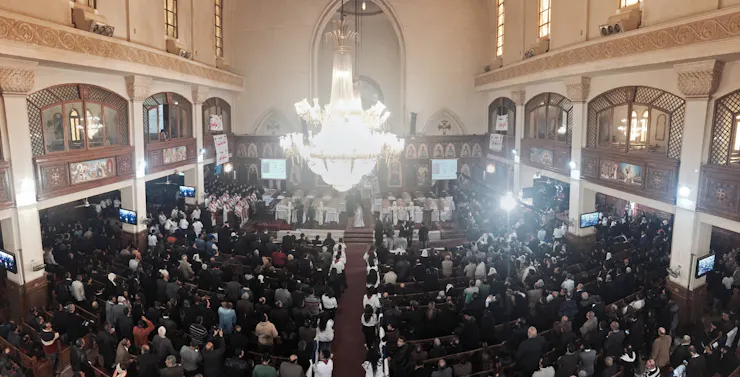 People standing in the pews of a large cathedral with several coffins laid out in the front.