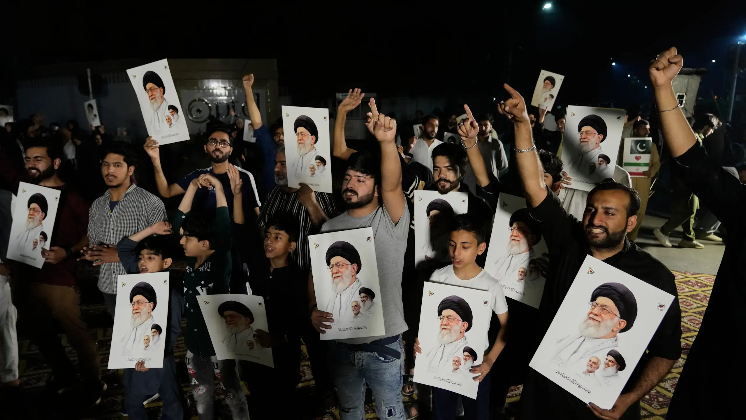 Several men, holding photos of Ayatollah Khamenei, raise their arms in protest.
