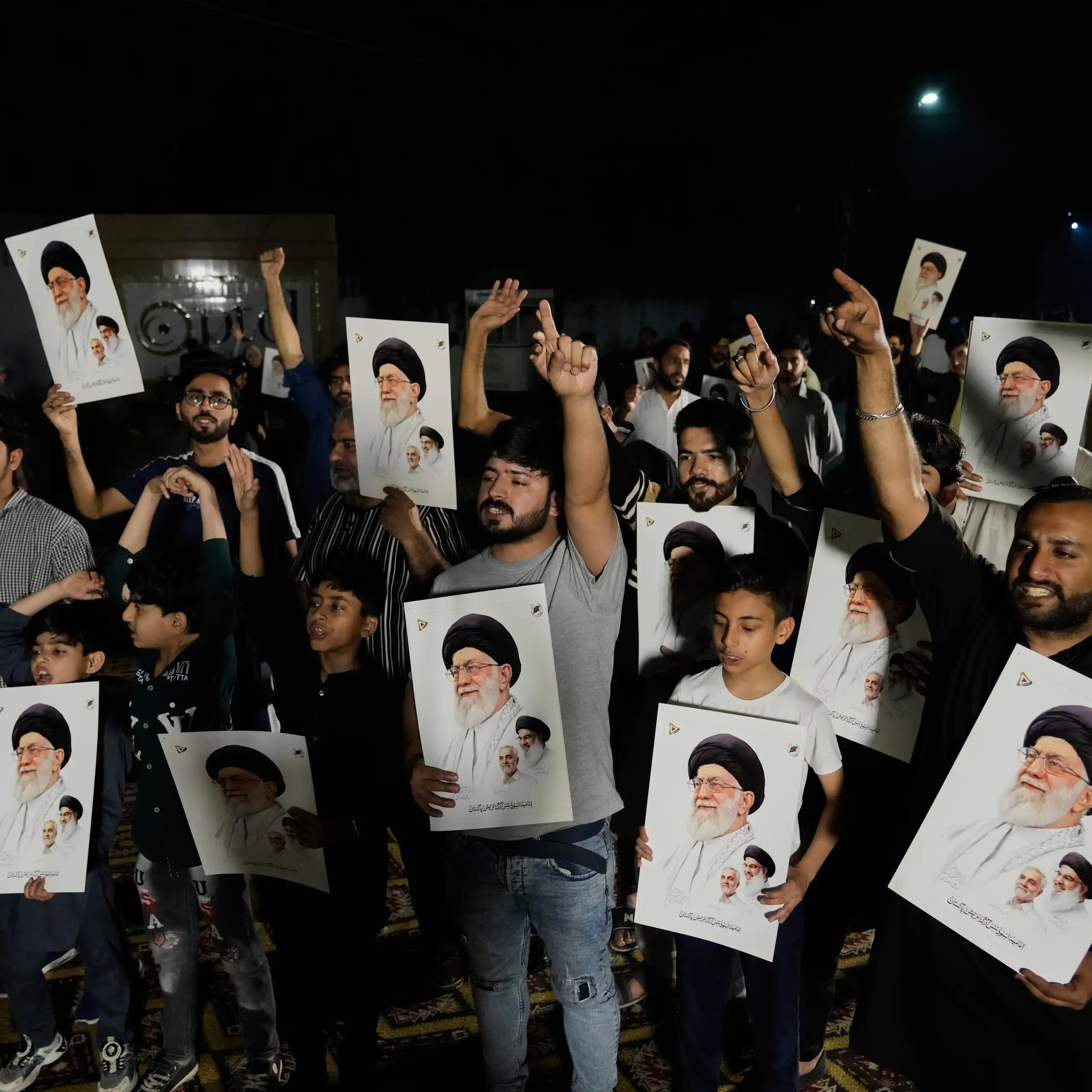 Several men, holding photos of Ayatollah Khamenei, raise their arms in protest.