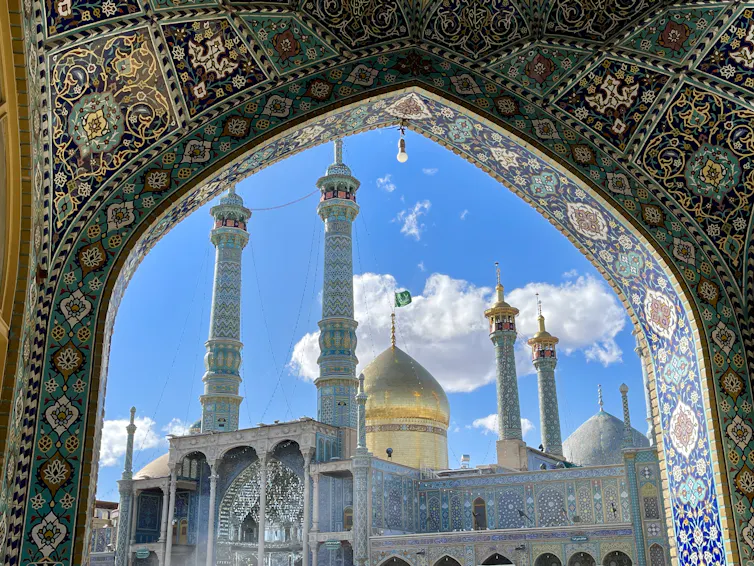 El dolor chiita por los ataques a las ciudades santas de Irán tiene profundas raíces históricas 1 La mezquita con su cúpula brillante y sus altos minaretes se puede ver a través de un arco con intrincados diseños coloridos.