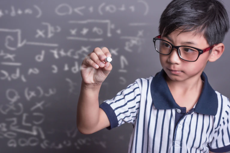 Schoolboy writing math formula on blackboard.
