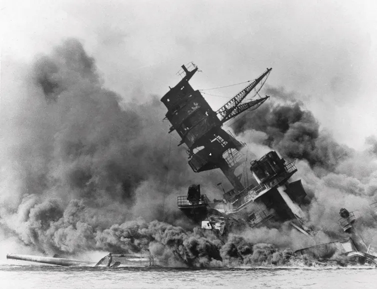 A black-and-white photo shows a sinking battleship engulfed in smoke.