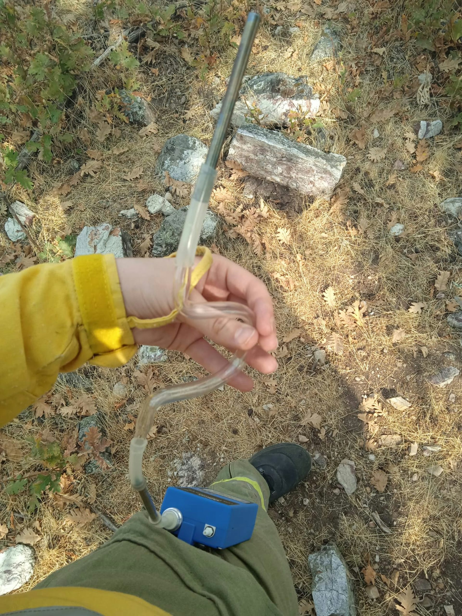 La mano sostiene un dispositivo compuesto por un cilindro y un tubo de plástico unido a una caja azul.