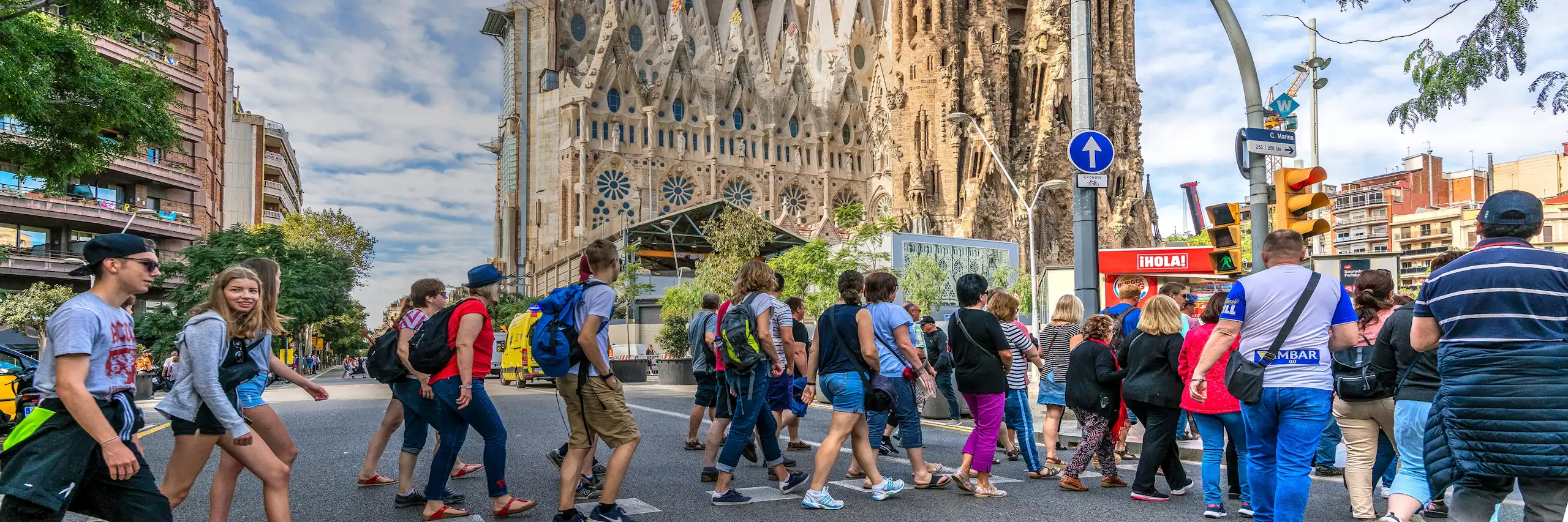 Molta gent creua un pas de vianants davant la Sagrada Família de Barcelona.