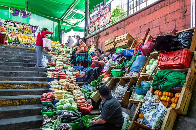 Vendedoras de frutas y verduras en una escalera dentro de un mercado.