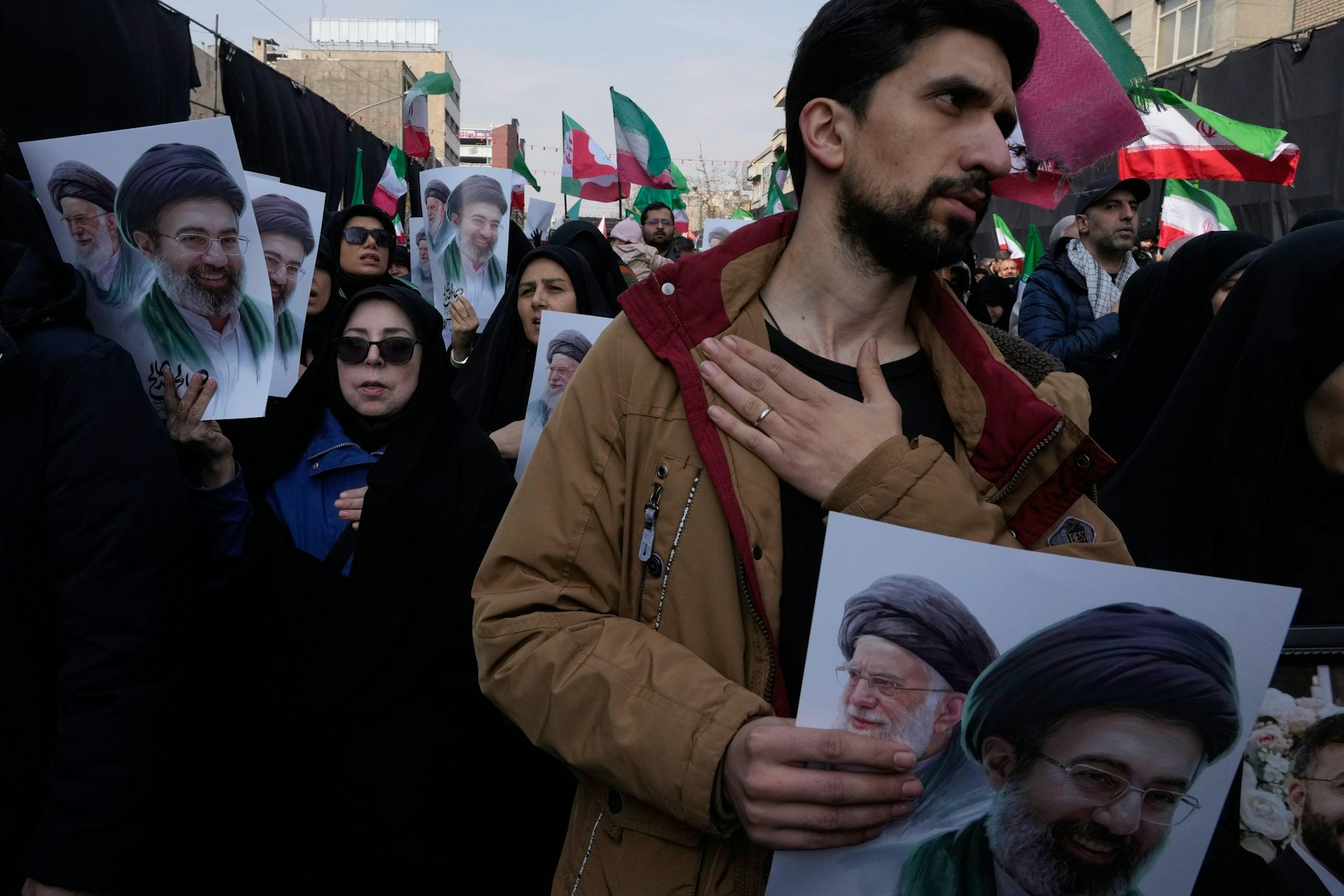 Iranians hold up pictures of the former supreme leader Ali Khamenei and his son Mojtaba while beating their chests, March 2026.