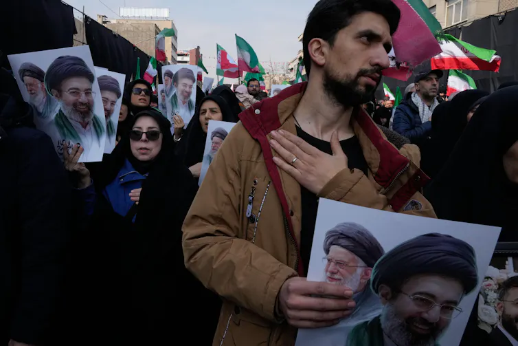Iranians hold up pictures of the former supreme leader Ali Khamenei and his son Mojtaba while beating their chests, March 2026.