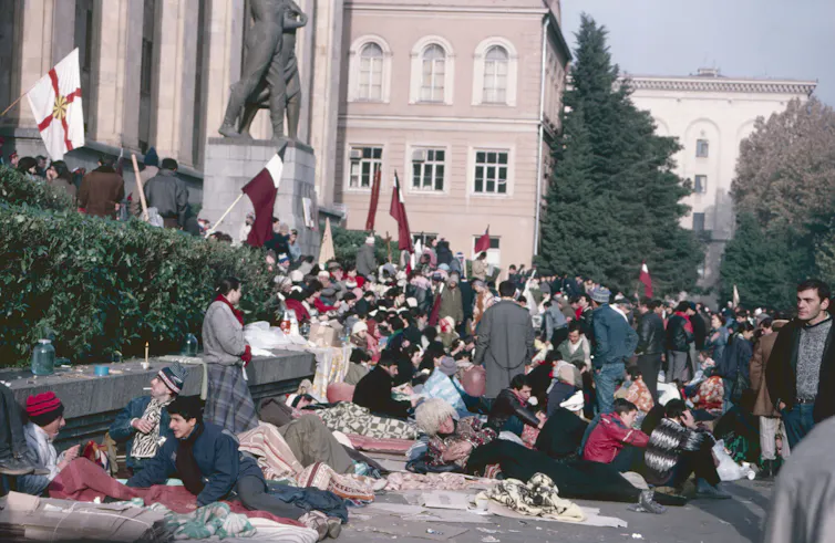 People engaged in a hunger strike lie on a pavement outside a parliamentary buidling.