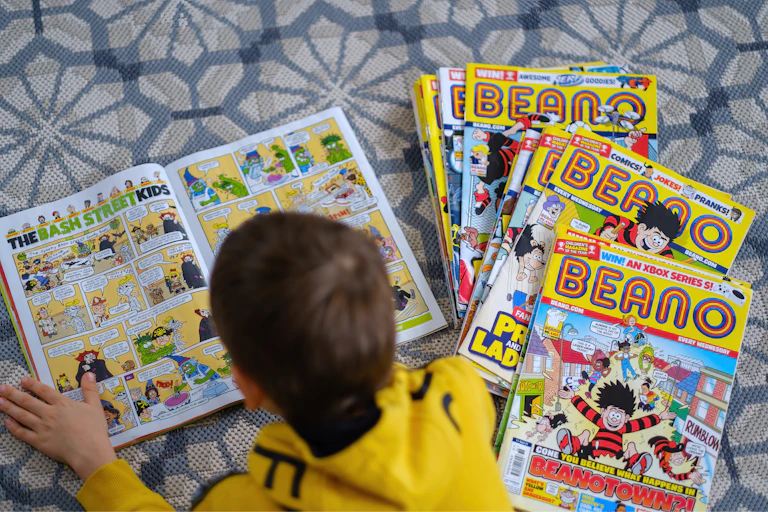 A boy reading copies of the Beano