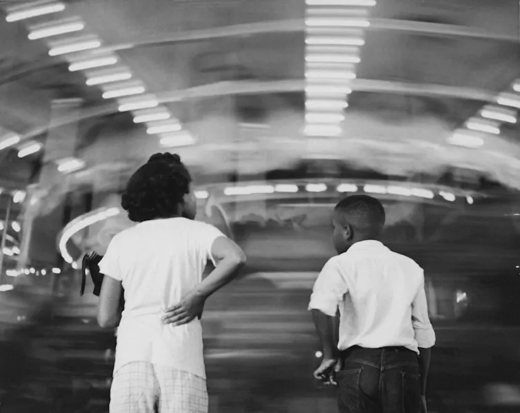 Black-and-white photo of girl and boy standing in front of whirling amusement ride