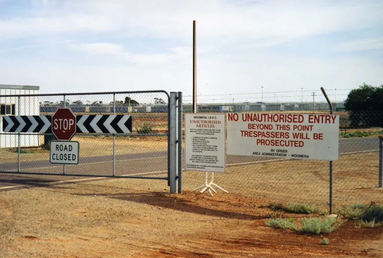 A photo of the front gate of a closed detention centre, with signs that read 'STOP', 'ROAD CLOSED' and 'NO UNAUTHORISED ENTRY'.