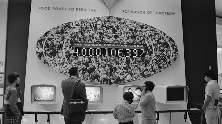 People listen at an exhibit displaying a population of just over 4 billion.
