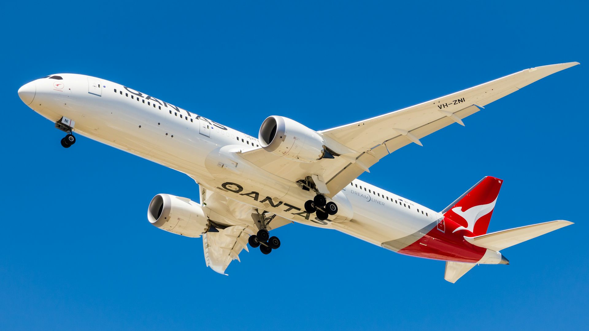A Boeing Dreamliner 787 Qantas plane against a bright blue sky.