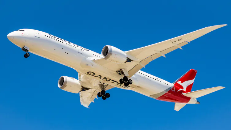 A Boeing Dreamliner 787 Qantas plane against a bright blue sky.