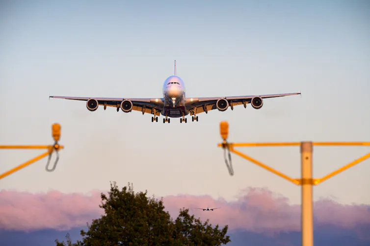 airbus a380 coming in to land at heathrow airport in london over trees and landing lights.