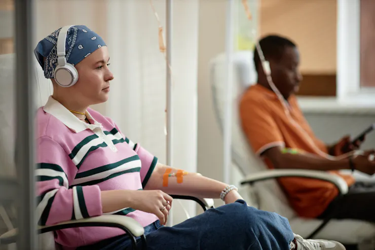 Two patients in chairs with IVs attached to their arms, wearing street clothes, headphones over their ears