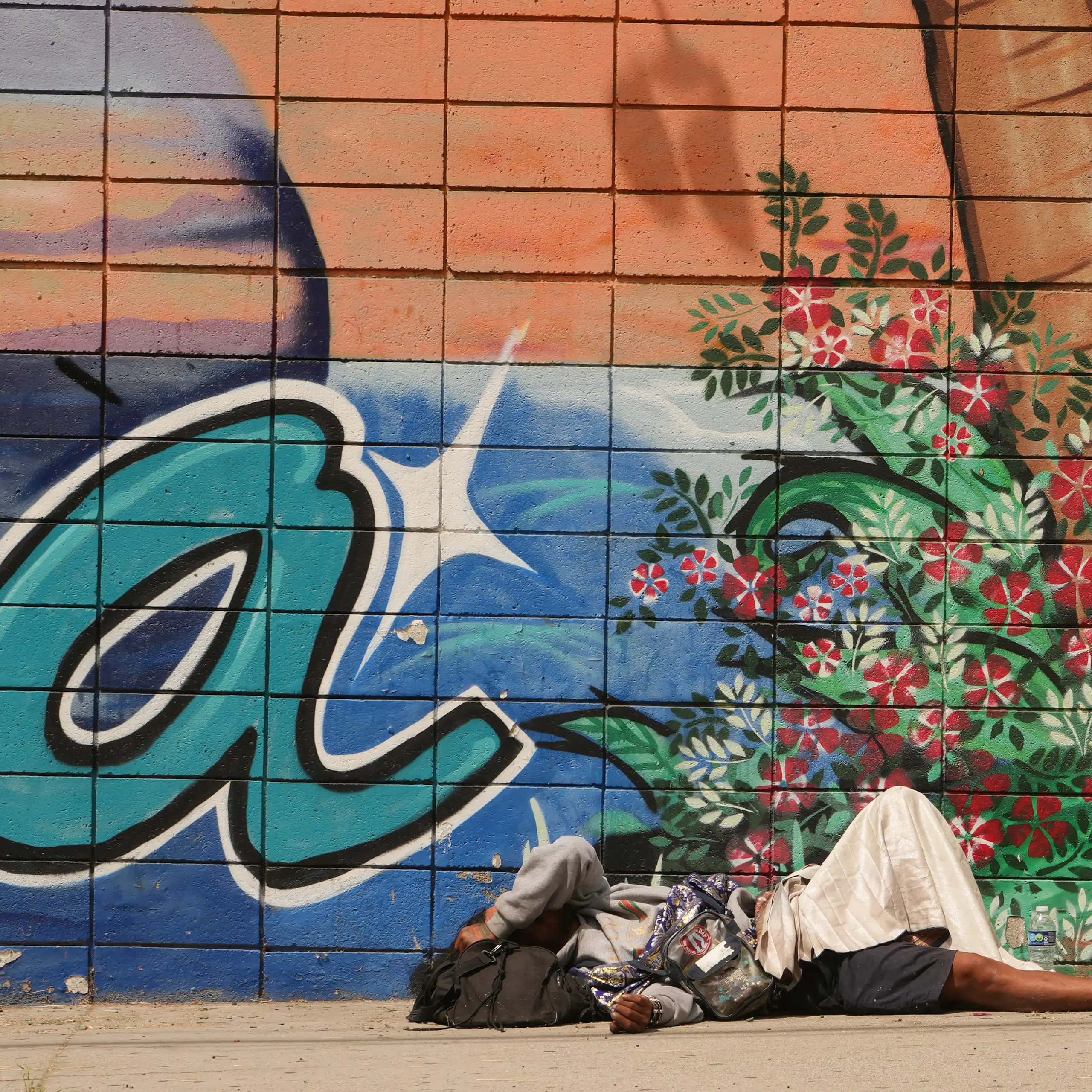 A homeless man lies on the sidewalk, next to artistic graffiti.
