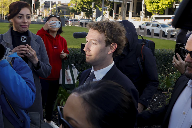 A man walking through a press pack, sunlight on his face.
